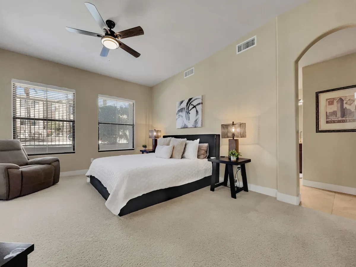 A cozy guest bedroom featuring a comfortable bed, large windows letting in natural light, an inviting armchair, and a nightstand. The room’s soft hues and serene decor evoke peace and relaxation.