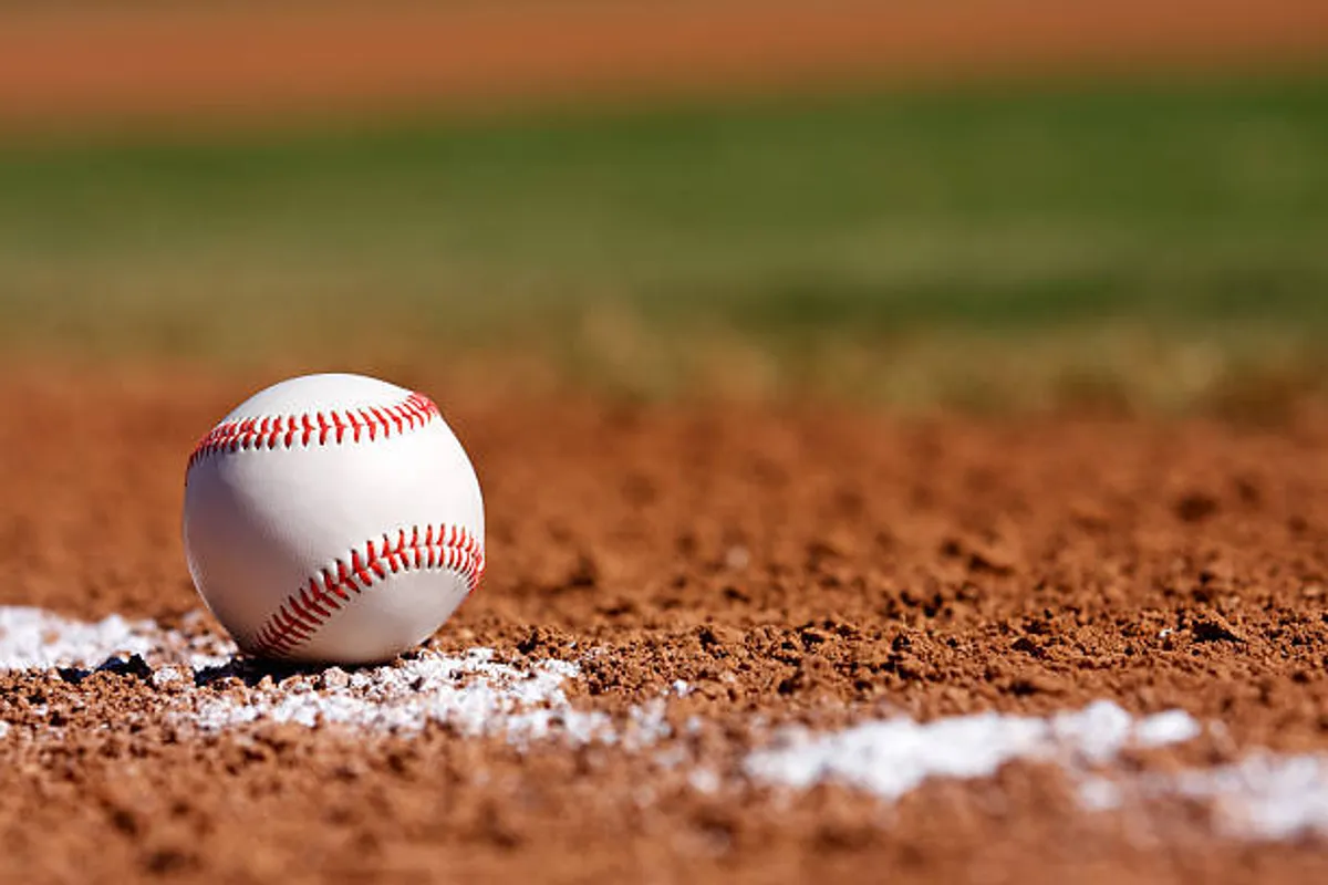 A close-up action shot of a baseball on a dirt infield, marked by a crisp white chalk line. The scene captures the anticipation and excitement of baseball, evoking the vibrancy of local spring training games and community sports.