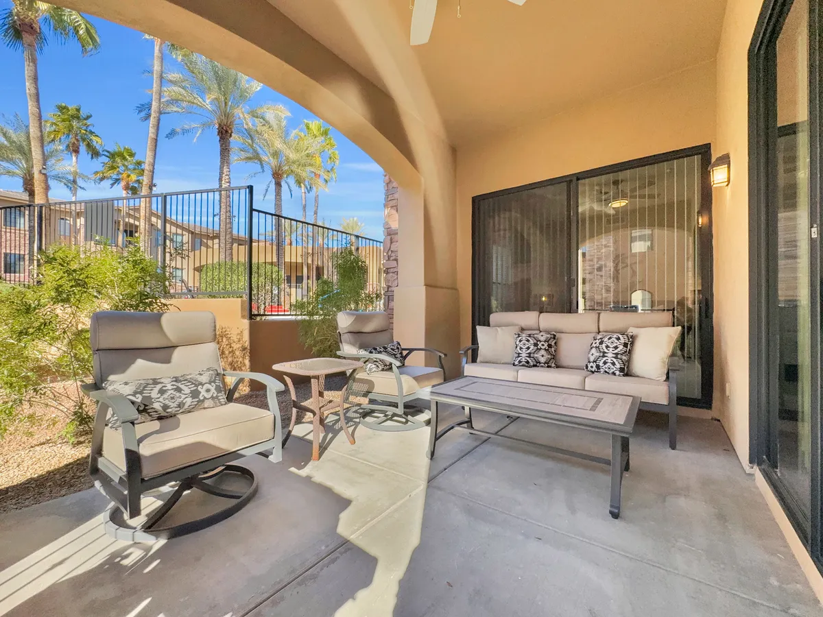 This exterior image features a cozy outdoor seating area with comfortable chairs, decorative pillows, and lush greenery, including palm trees. The tranquil atmosphere is inviting for relaxing, reading, or connecting with friends against a backdrop of natural beauty.