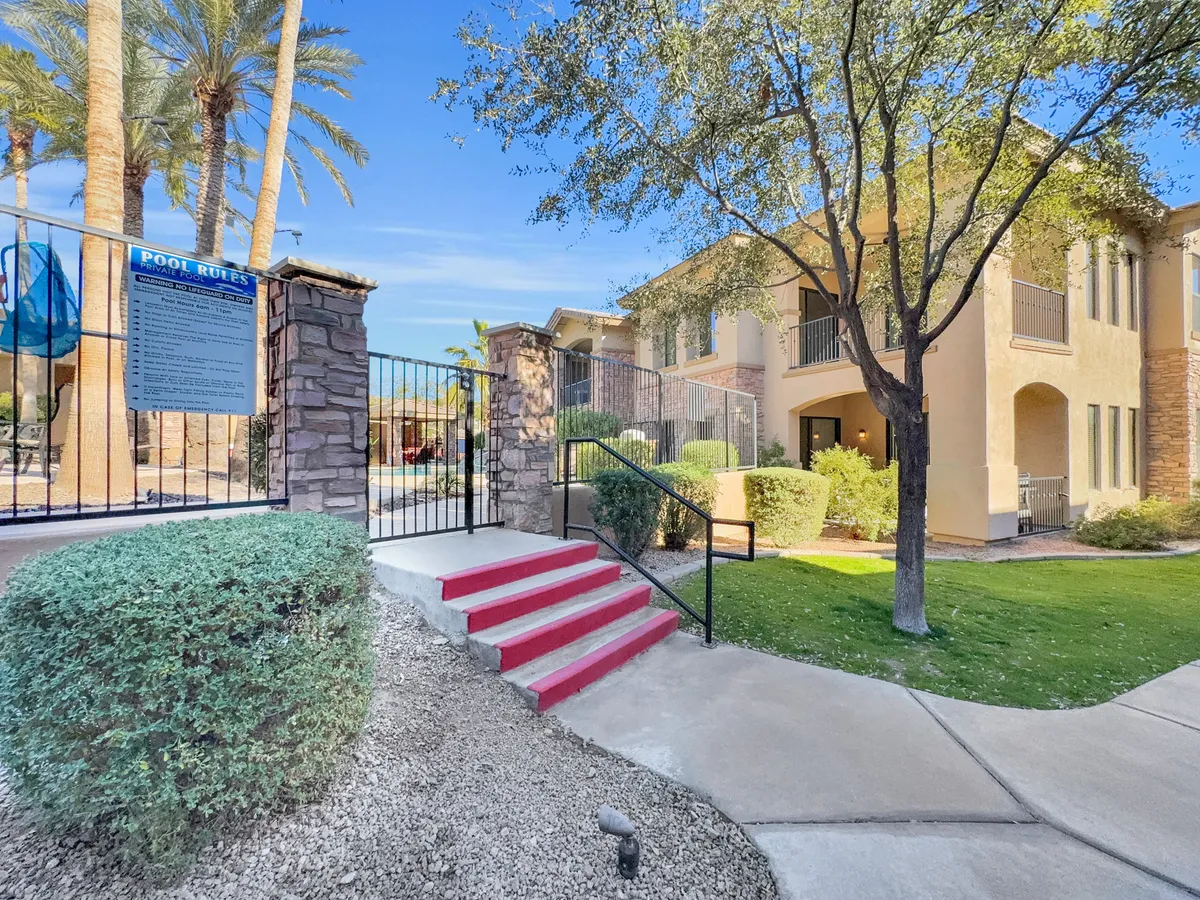 An exterior shot of a vibrant poolside area, with a red stairway, palm trees, lush landscaping, and signage. The setting is both lively and inviting, evoking a sense of leisure and sunny weather typical of Arizona.