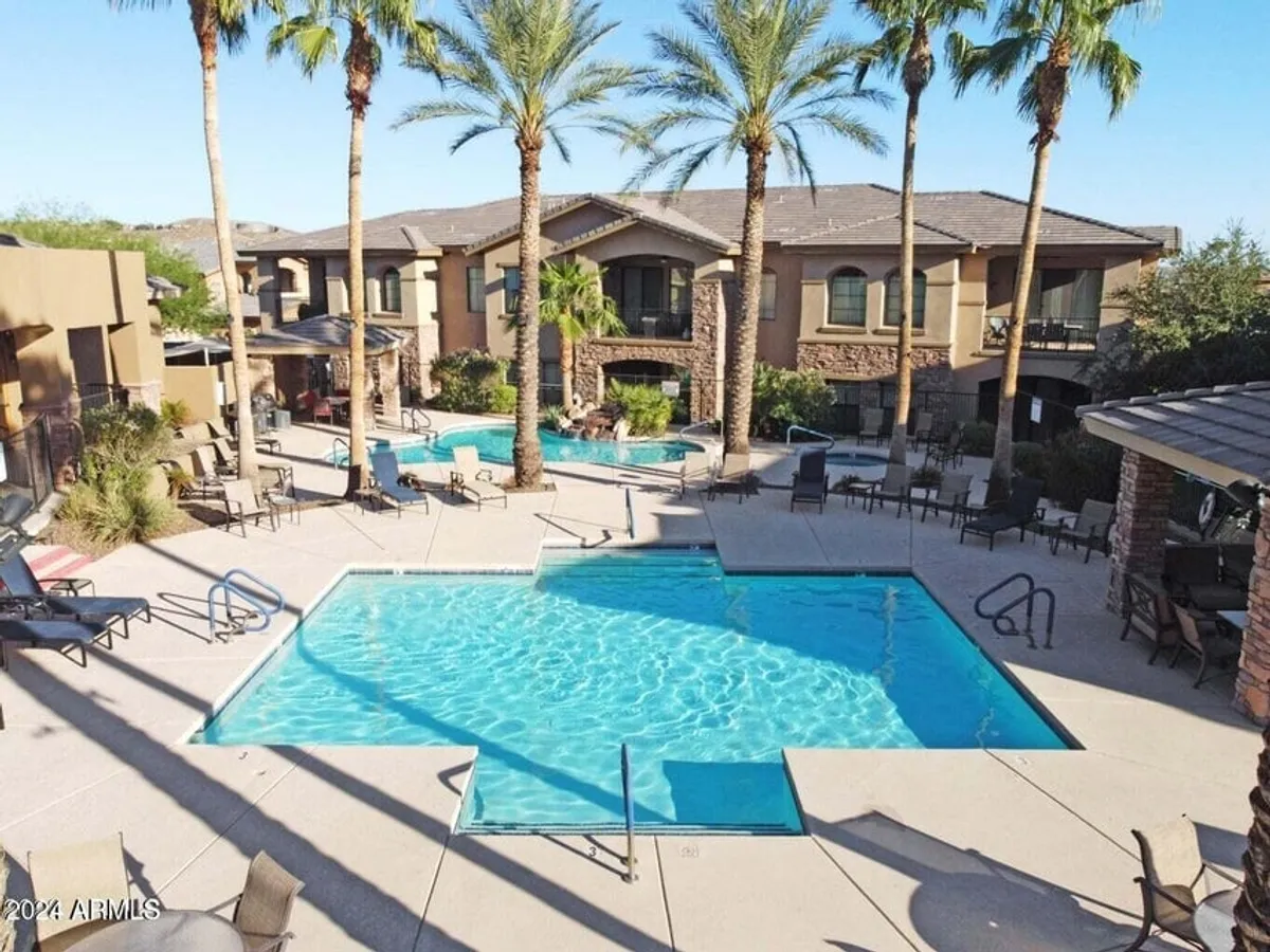 A sun-drenched swimming pool surrounded by palm trees and lounge chairs, with the building's facade visible in the background. The space feels open, inviting, and perfect for socializing or relaxing by the water.